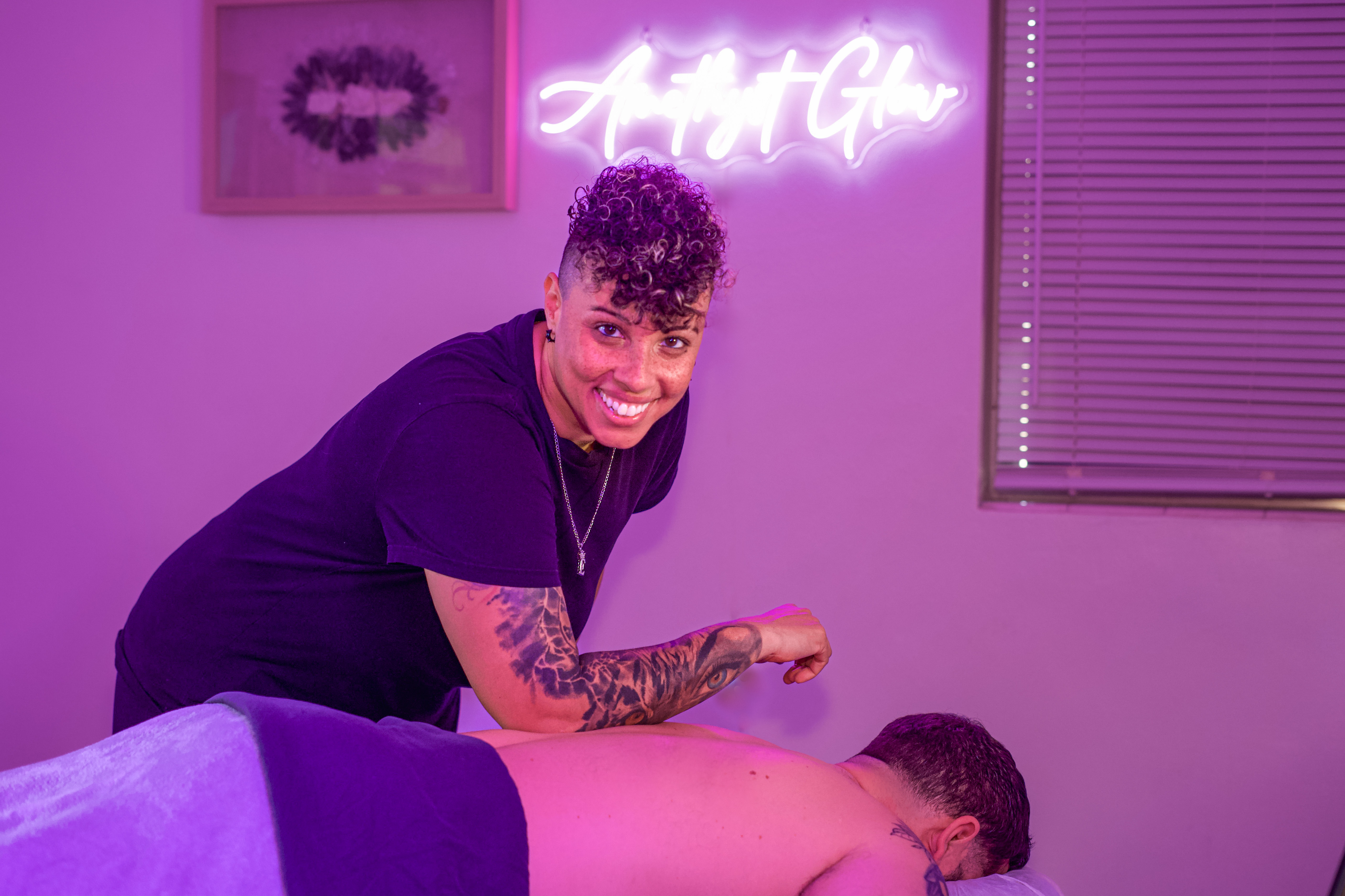 Massage therapist working under Amethyst Glow neon sign
